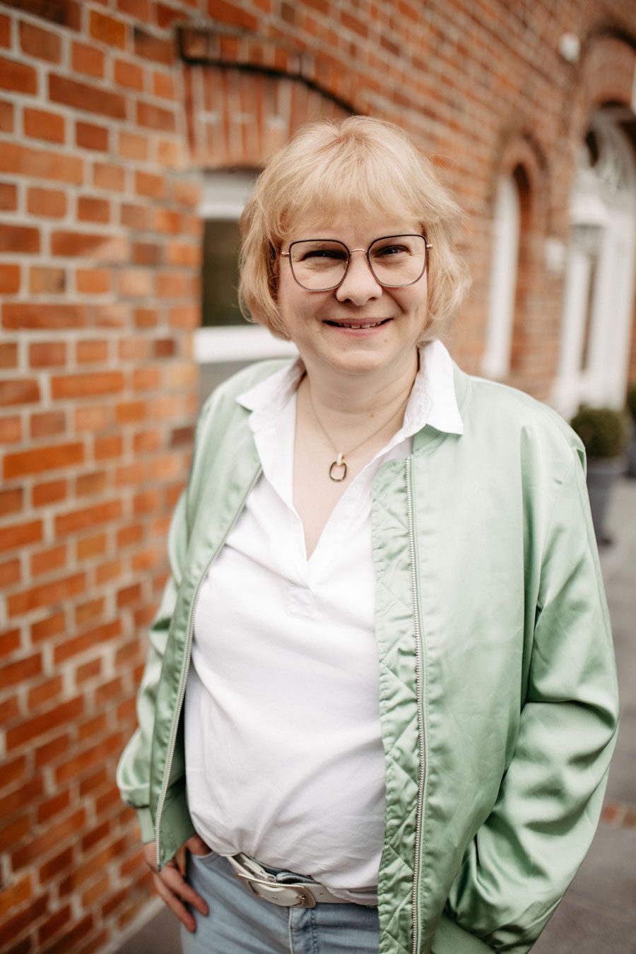 Eine Frau in einem rosa Hemd und mit Brille sitzt auf einem Stuhl in einem Salon.