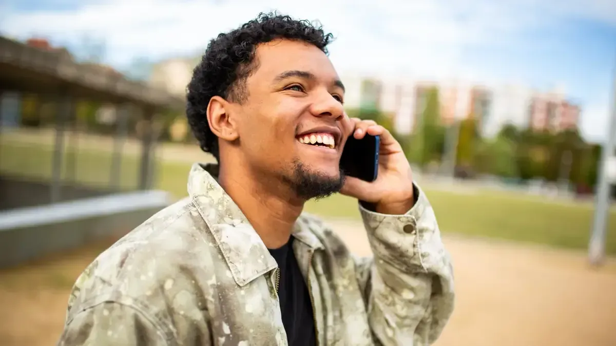 Persona sonriente con chaqueta de camuflaje hablando por un teléfono celular al aire libre.