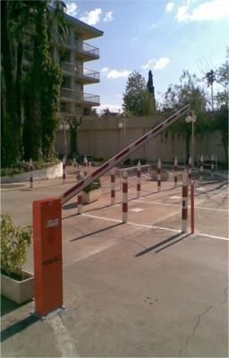 Una barrera roja en un estacionamiento con un edificio al fondo.
