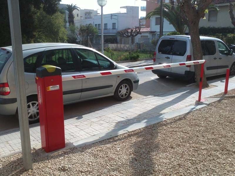 Un coche blanco está aparcado detrás de una barrera roja.