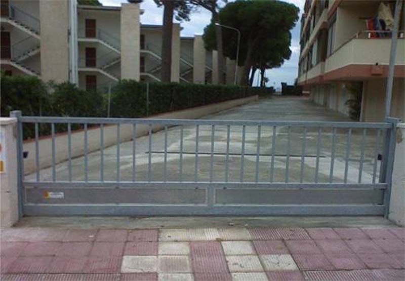 Una puerta corrediza se abre a un camino de entrada que conduce a un edificio.