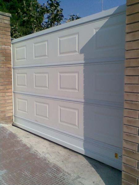 Una puerta de garaje blanca está frente a una pared de ladrillos.