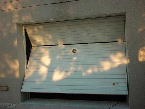 Una puerta de garaje blanca está abierta y las sombras de los árboles se proyectan en la pared.