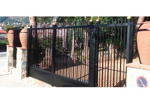 Una puerta de hierro forjado negro está rodeada de plantas y árboles en macetas.