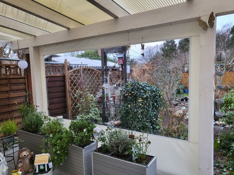 Eine Terrasse mit Pflanzgefäßen voller Pflanzen und Blick auf einen Garten.