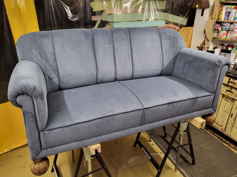 In einem Zimmer steht ein blaues Sofa auf einem Holztisch.