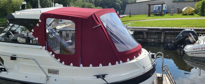 Ein weißes Boot mit einem roten Verdeck liegt in einem Yachthafen vor Anker.