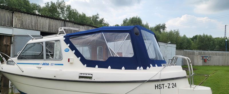 Ein weißes Boot mit blauem Verdeck liegt auf einer Rasenfläche.