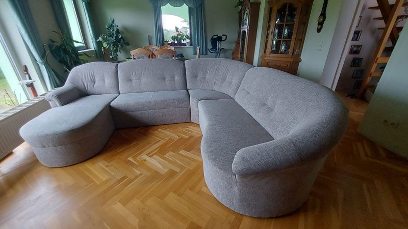 In einem Wohnzimmer steht auf einem Holzboden ein großes Sofa.