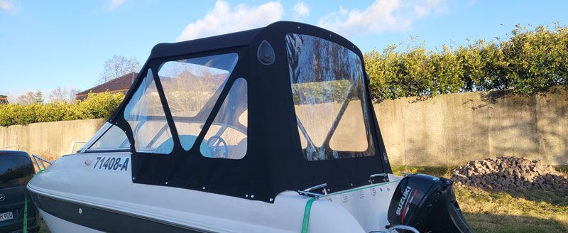 Vor einem Zaun steht ein weißes Boot mit schwarzem Verdeck.