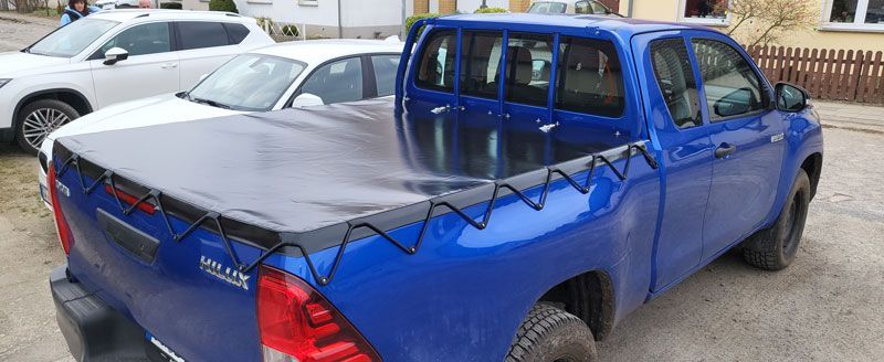 Ein blauer Lastwagen mit schwarzer Ladeflächenabdeckung steht neben einem weißen Auto.