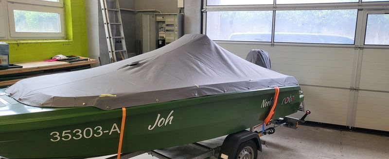 Ein grünes Boot mit einer Abdeckung steht in einer Garage.