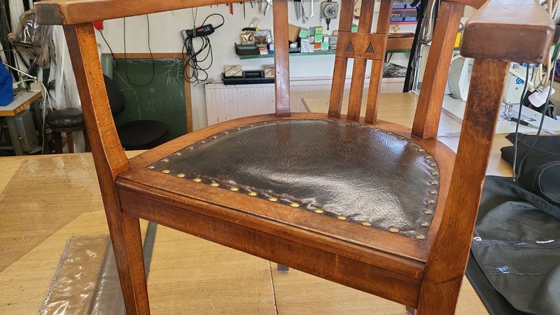 Auf einem Holztisch steht ein Holzstuhl mit Ledersitz.