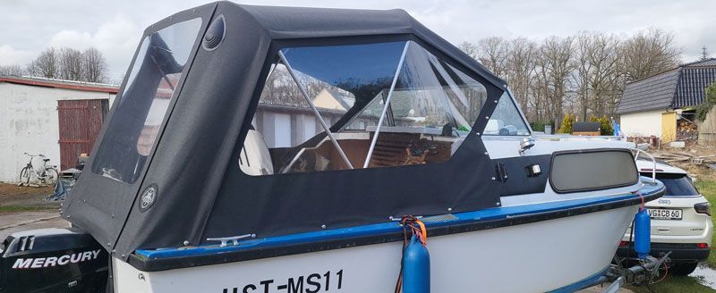 Ein Boot mit einem Verdeck ist neben einem Auto geparkt.