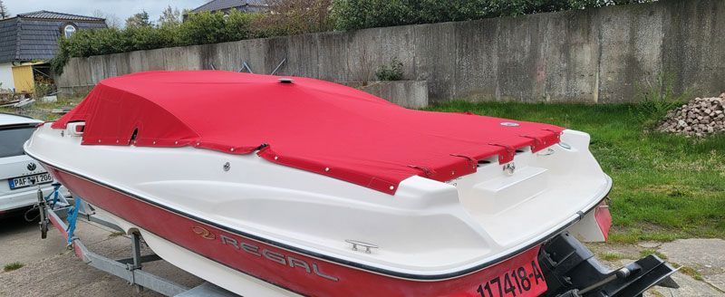 Auf einem Anhänger steht ein rot-weißes Boot mit einer roten Abdeckung.