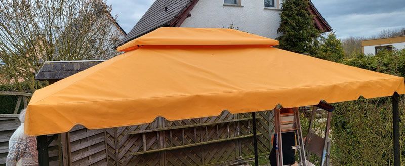 Vor einem Haus steht ein orangefarbenes Vordach.