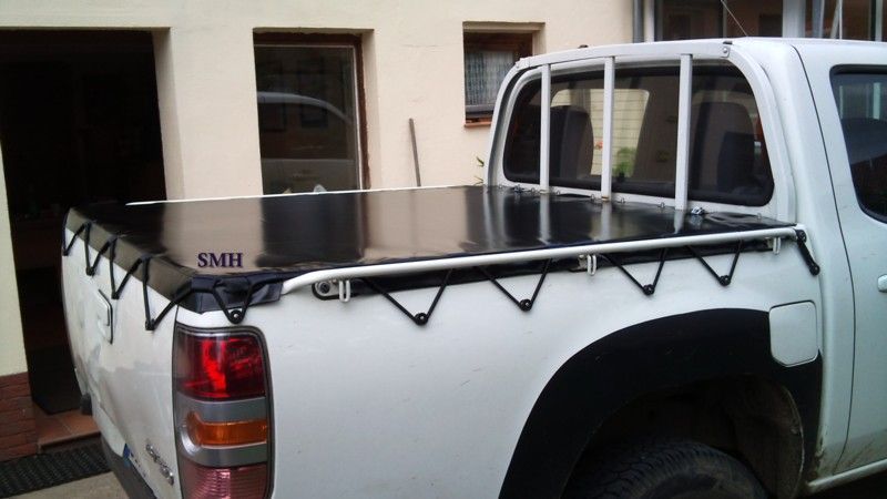 Ein weißer LKW mit einer schwarzen Abdeckung auf der Ladefläche steht vor einem Gebäude