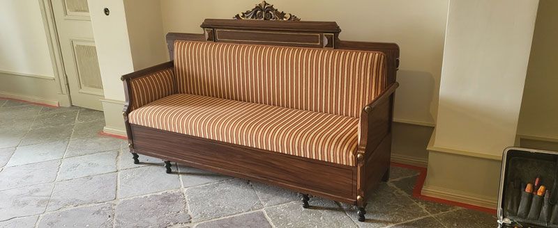 In einem Flur steht ein Holzsofa mit gestreiftem Kissen.