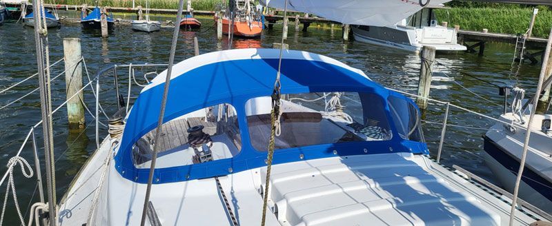 Ein Segelboot mit blauem Verdeck liegt in einem Yachthafen vor Anker.