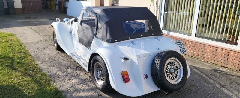 Ein weißes Auto mit schwarzem Dach ist vor einem Backsteingebäude geparkt.