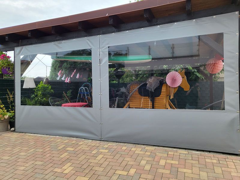 Auf einer gepflasterten Auffahrt steht ein graues Zelt mit einem durchsichtigen Fenster.