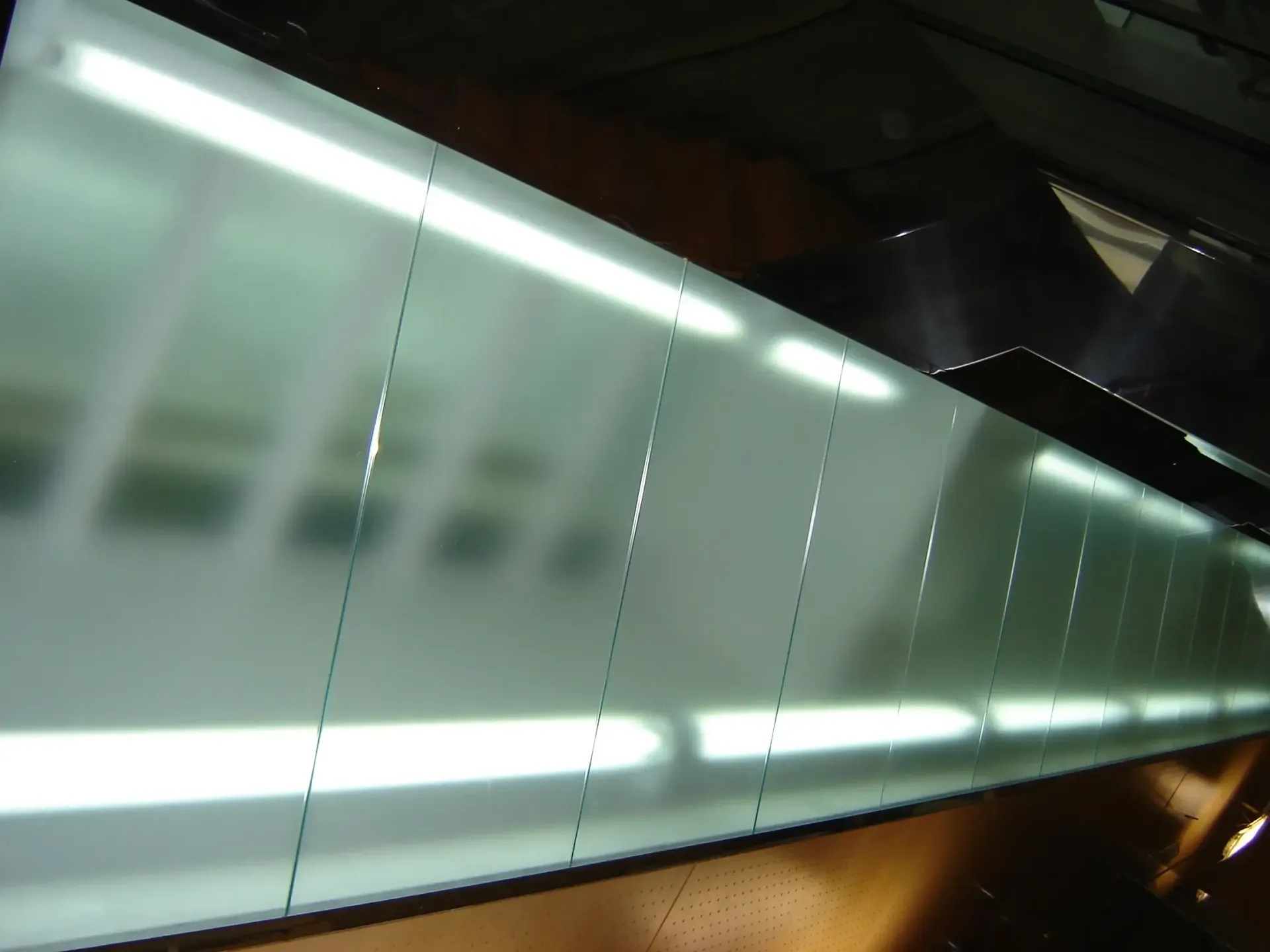 Vista diagonal de una barandilla de vidrio esmerilado con luces brillantes y reflejos difuminados en un interior moderno.