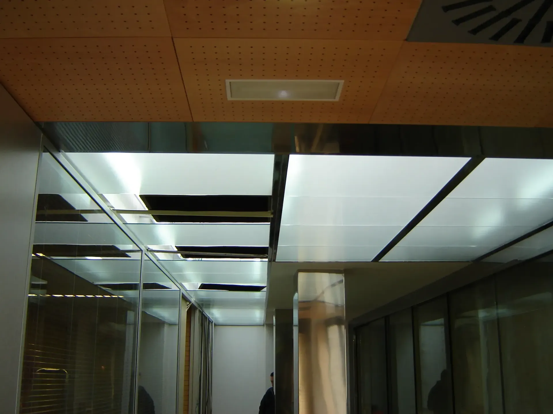 Pasillo de oficina con paredes espejadas, paneles en el techo y tragaluces luminosos.