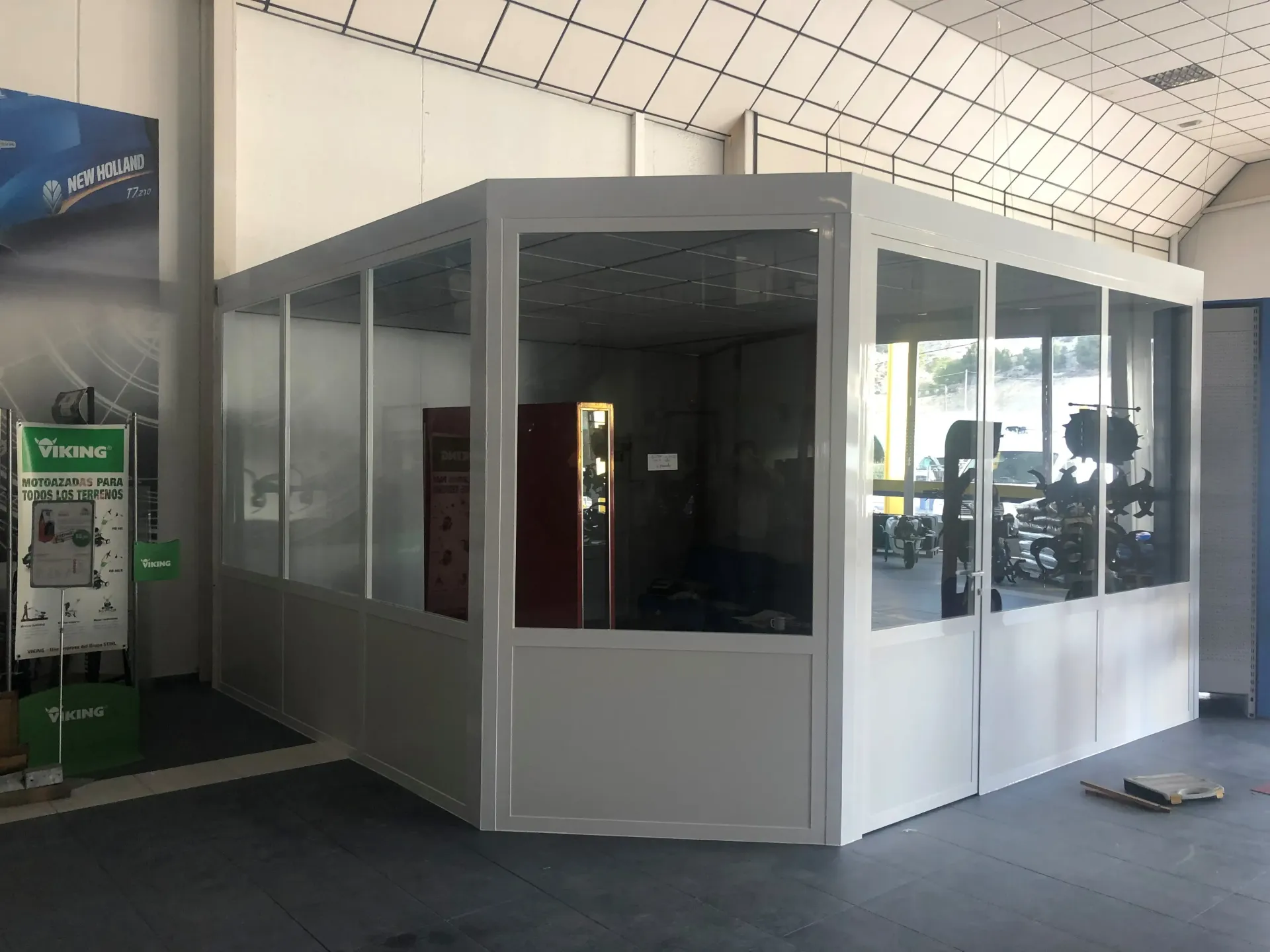 Cabina con paredes de cristal en una moderna terminal interior, con paneles blancos y un soporte para carteles cerca.