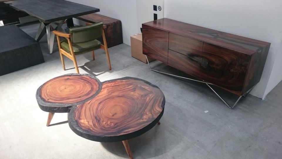 Ausstellung von Holzmöbeln: Couchtisch, Beistelltisch, Schrank, Tisch mit Bank und grüner Stuhl.