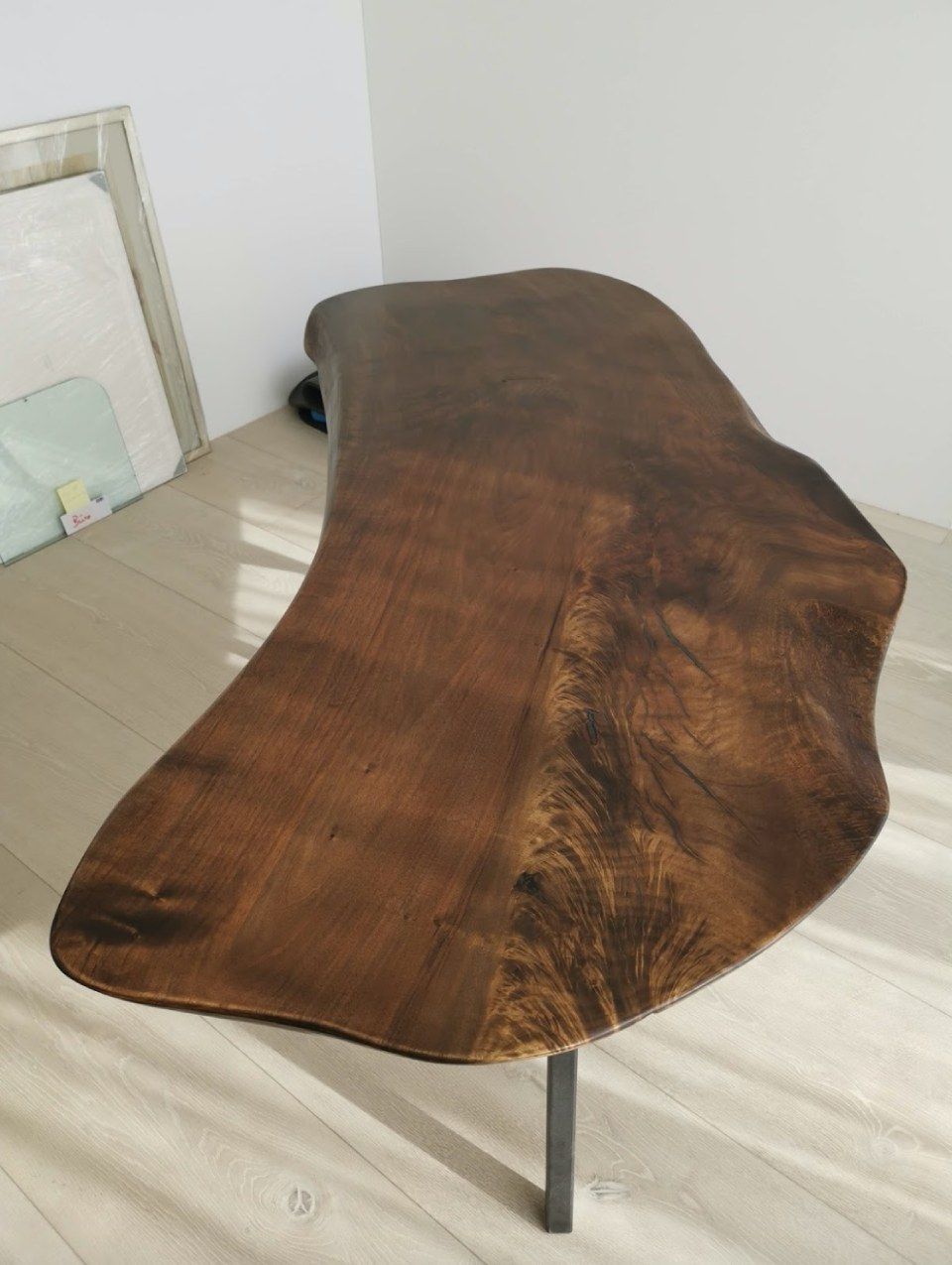 Ein brauner Holztisch mit natürlicher Baumkante und dunkler Oberfläche, getragen von Metallbeinen, steht auf einem hellen Holzboden.