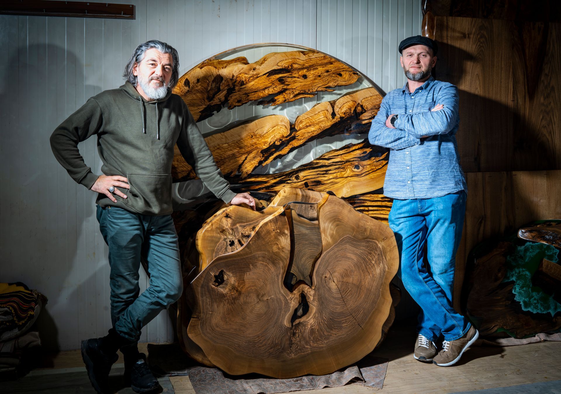 Ein Mann schleift in einer Werkstatt eine grosse, unregelmässige Holzplatte. Ein Werkstattsauger ist angeschlossen.