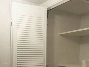 Un armario blanco con persianas y estantes en un baño.