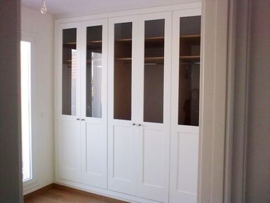 Un armario blanco con puertas de cristal y estantes en una habitación.