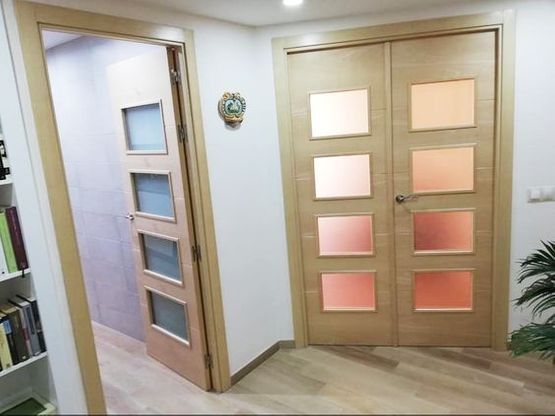 Un pasillo con dos puertas y un estante con libros encima.
