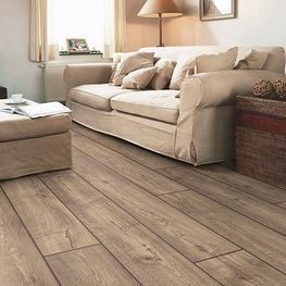 Una sala de estar con sofá, otomana, mesa y piso de madera.