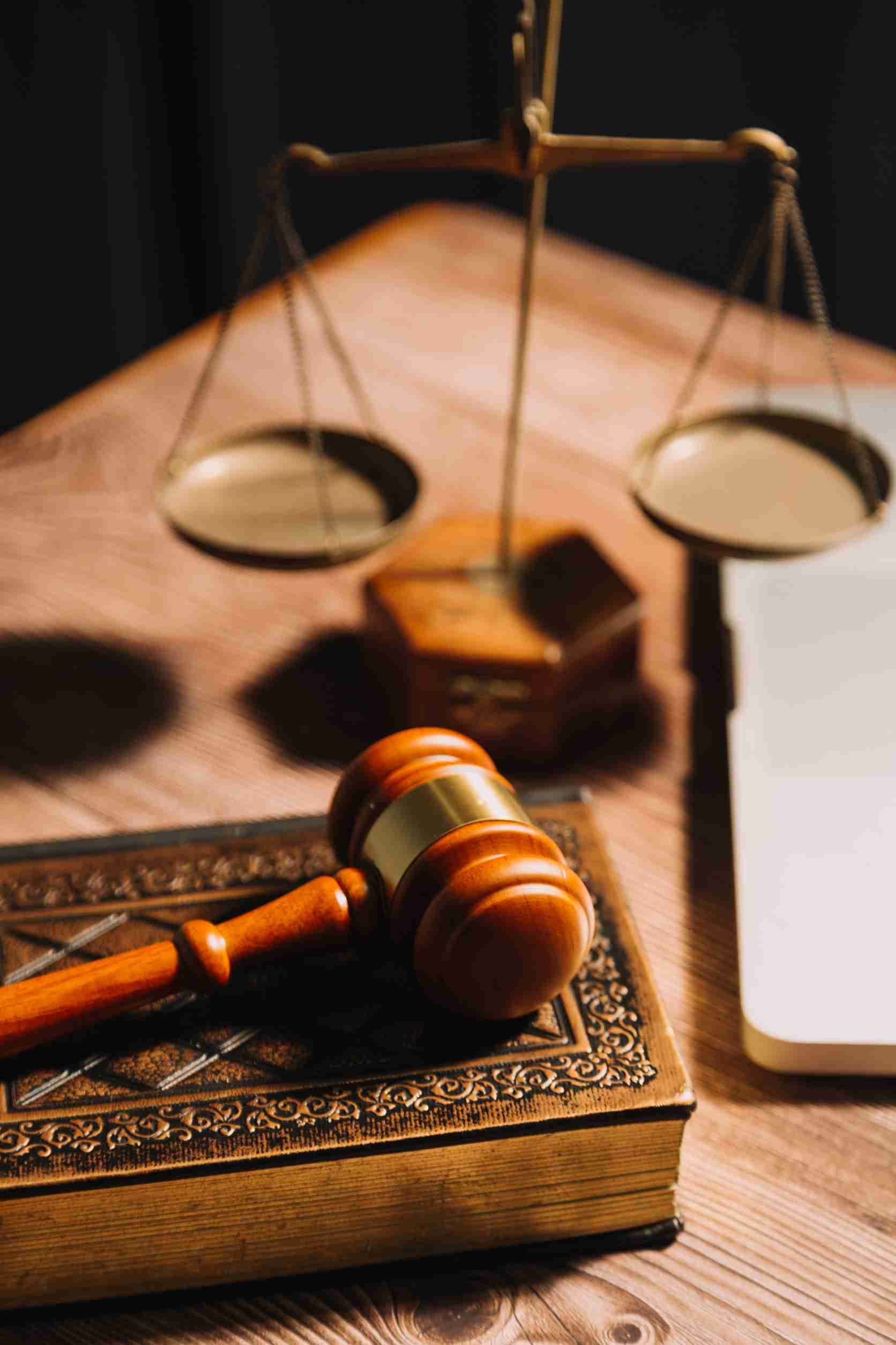 Mazo y balanza de la justicia sobre un escritorio de madera, con un libro y un bloc de notas cerca.