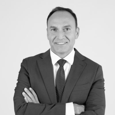 Hombre de traje con los brazos cruzados, sonriendo a la cámara.