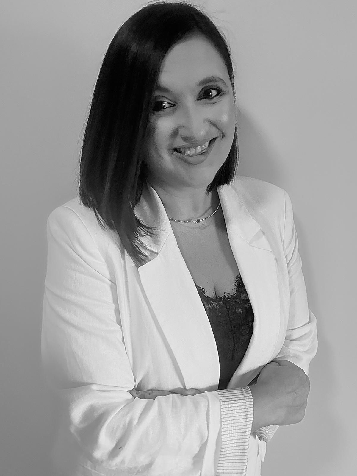 Mujer con camisa blanca con volantes sonríe a la cámara; retrato en blanco y negro.