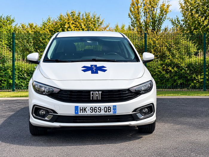 Gros plan sur le phare avant et la calandre d’une voiture blanche, avec des autocollants bleus sur le capot et l’aile