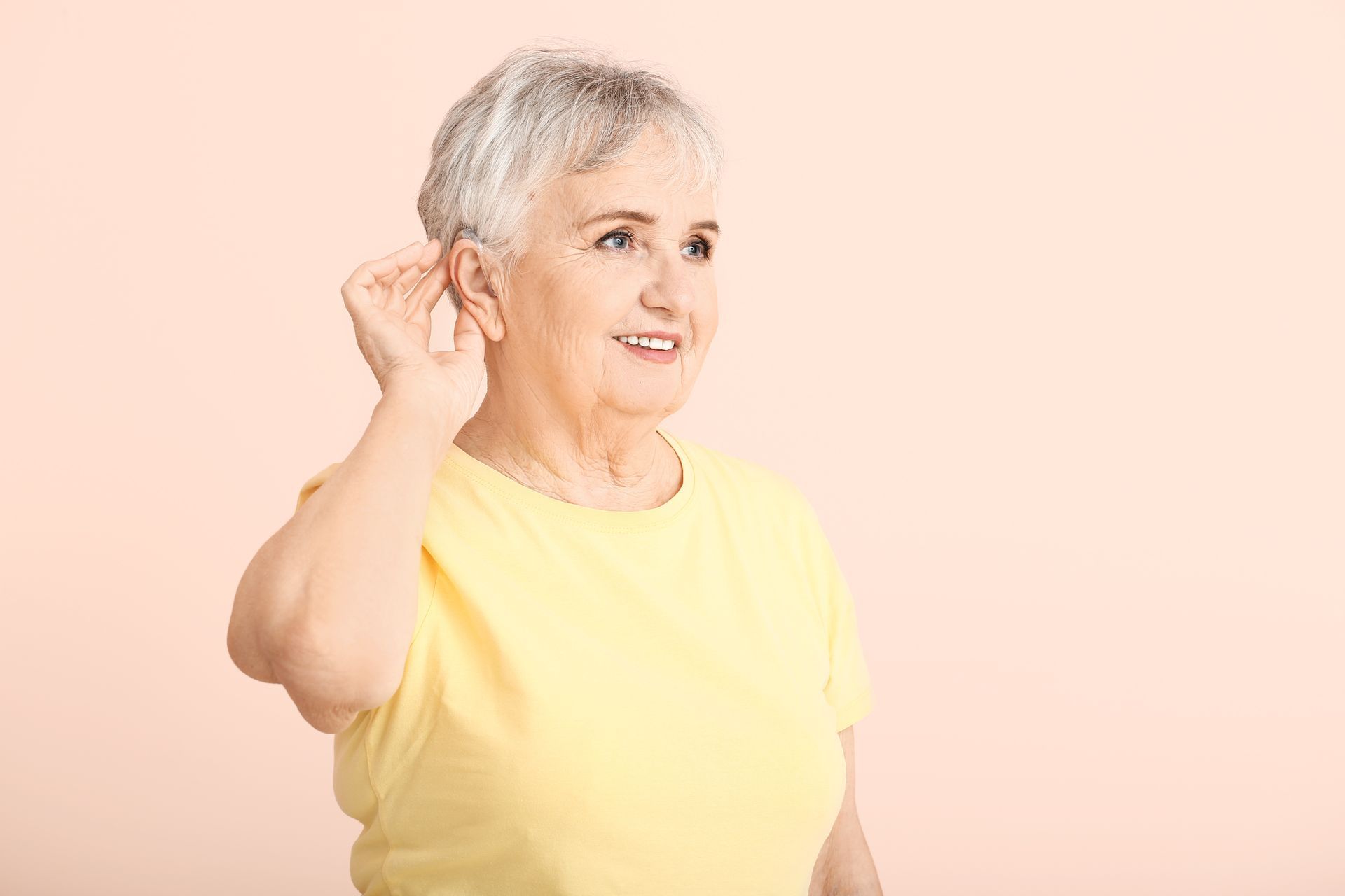 Femme âgée mettant une main derrière son oreille pour toucher son appareil auditif