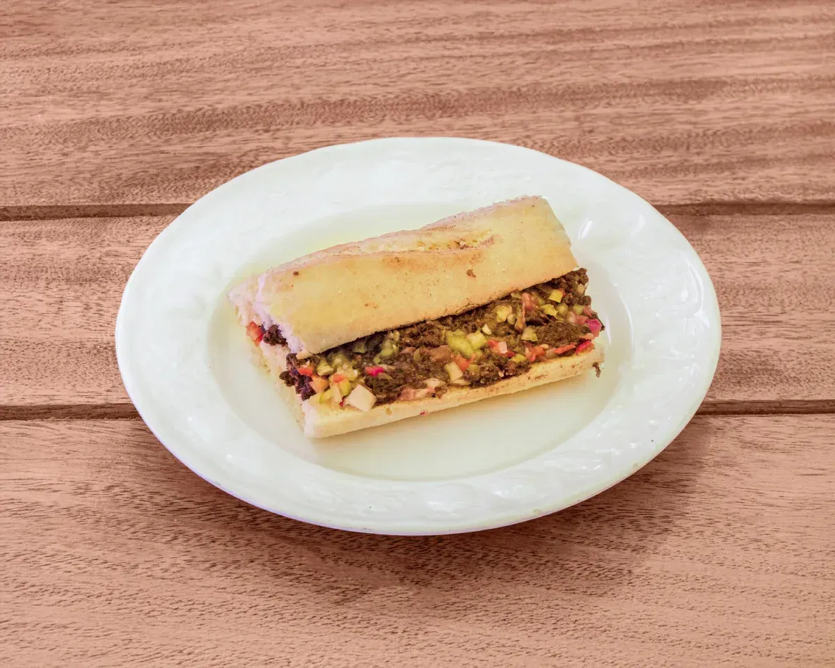 Sándwich servido en un plato blanco sobre una superficie de madera marrón. El sándwich está relleno.