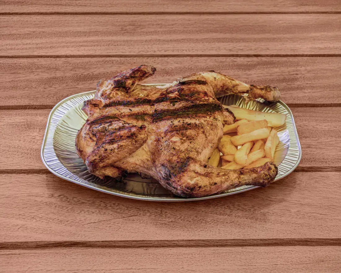 Pollo a la parrilla con patatas fritas en una bandeja de plata, sobre una mesa de madera.