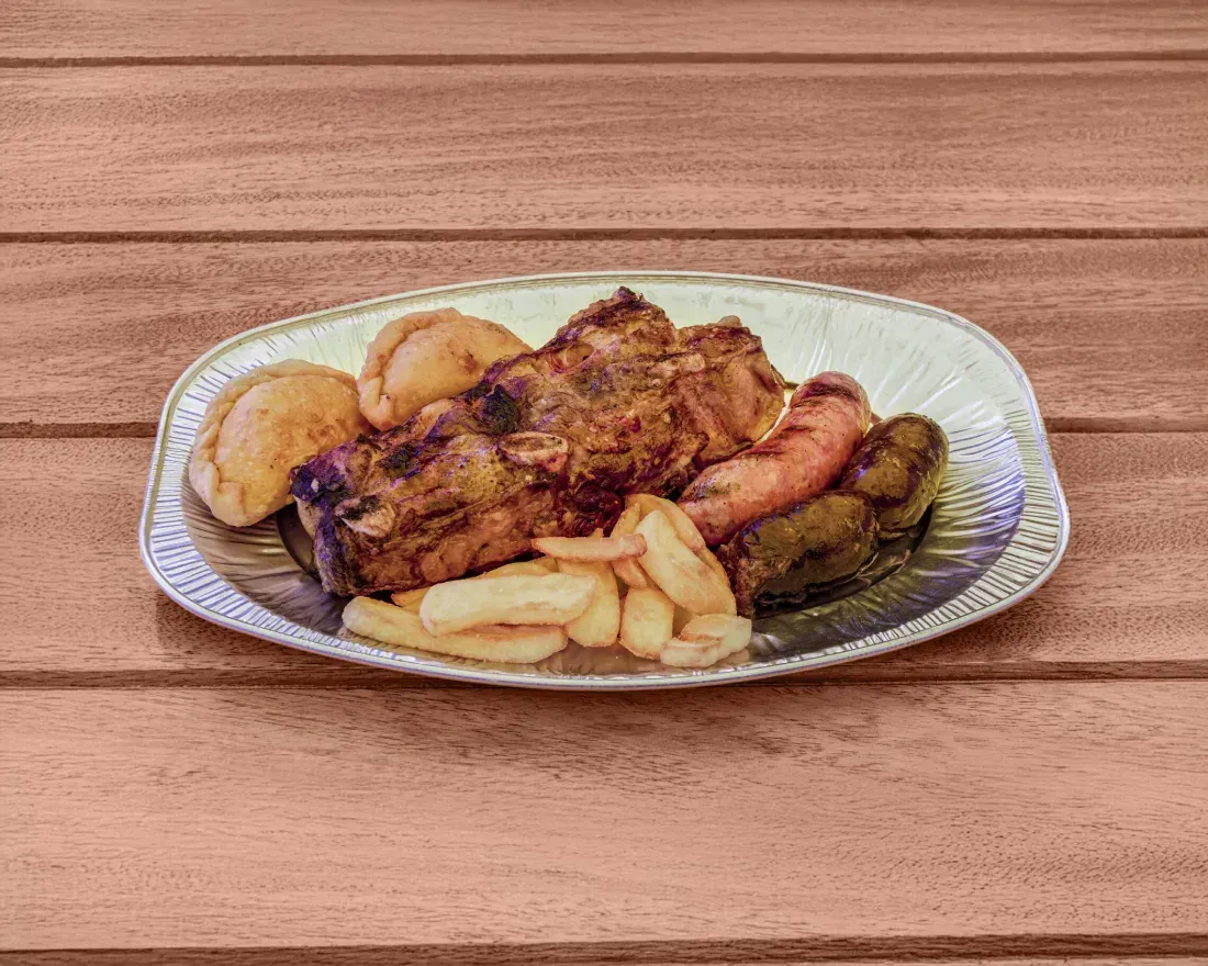 Carne asada con patatas, zanahorias y patatas fritas en una bandeja de plata, sobre una mesa de madera.