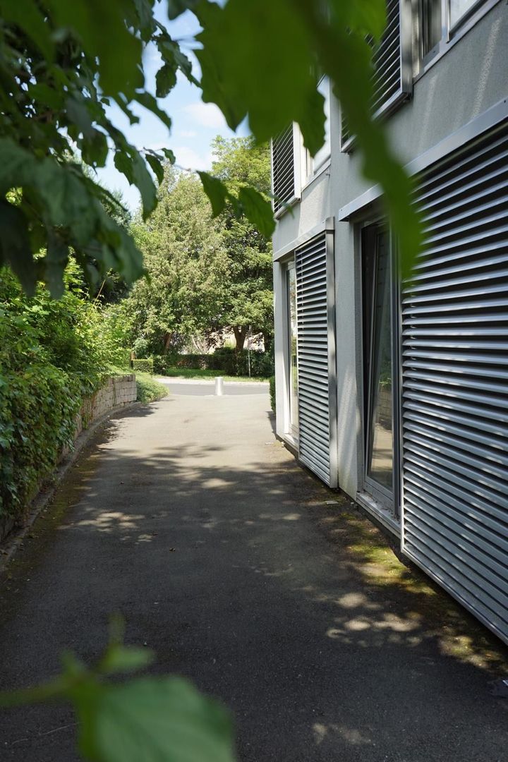 Ein Gehweg, der zu einem Gebäude führt, im Hintergrund sind viele Bäume zu sehen.