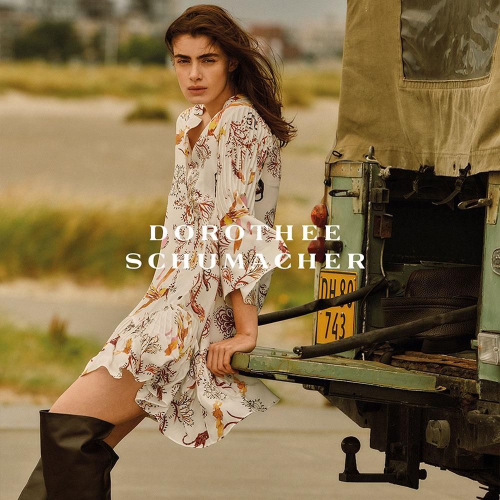 Eine Frau im Kleid lehnt an der Rückseite eines Fahrzeugs.