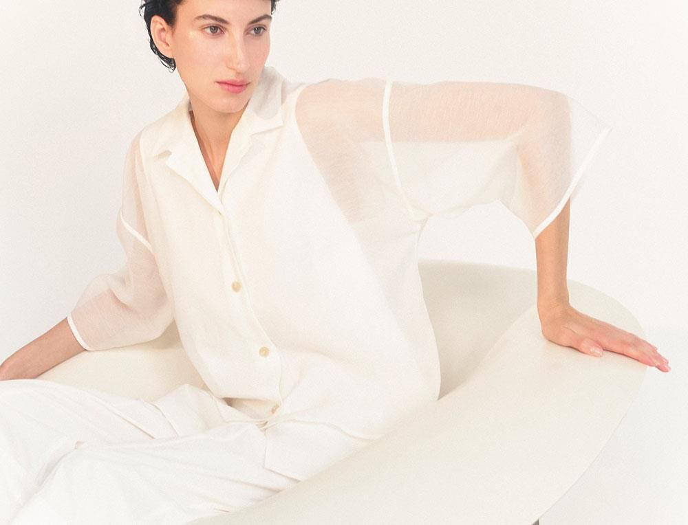 Eine Frau in einem weißen Hemd und weißen Hosen sitzt auf einer weißen Fläche.