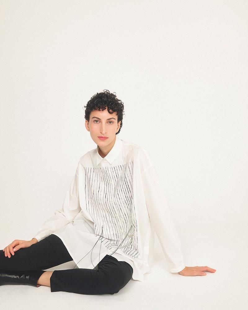 Eine Frau mit einem weißen Hemd und einer schwarzen Hose sitzt auf dem Boden.