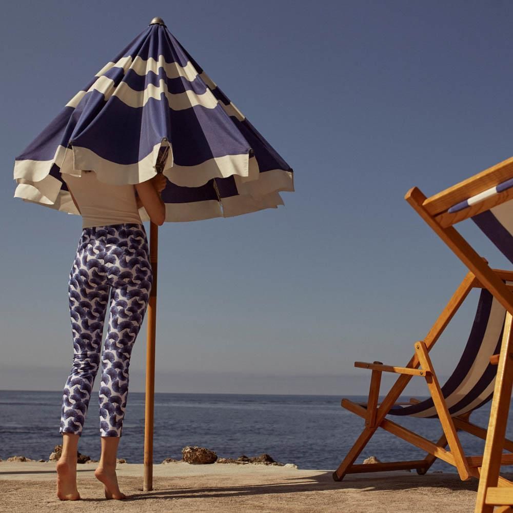 Eine Frau steht unter einem blau-weiß gestreiften Sonnenschirm am Strand
