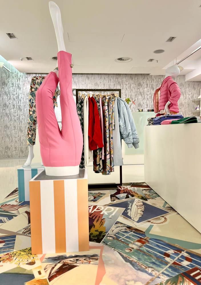 Eine rosa Schaufensterpuppe steht in einem Geschäft und an Kleiderständern hängt Kleidung.