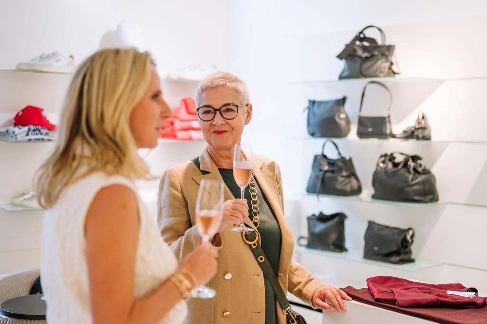Zwei Frauen stehen in einem Geschäft nebeneinander und halten Weingläser in den Händen.